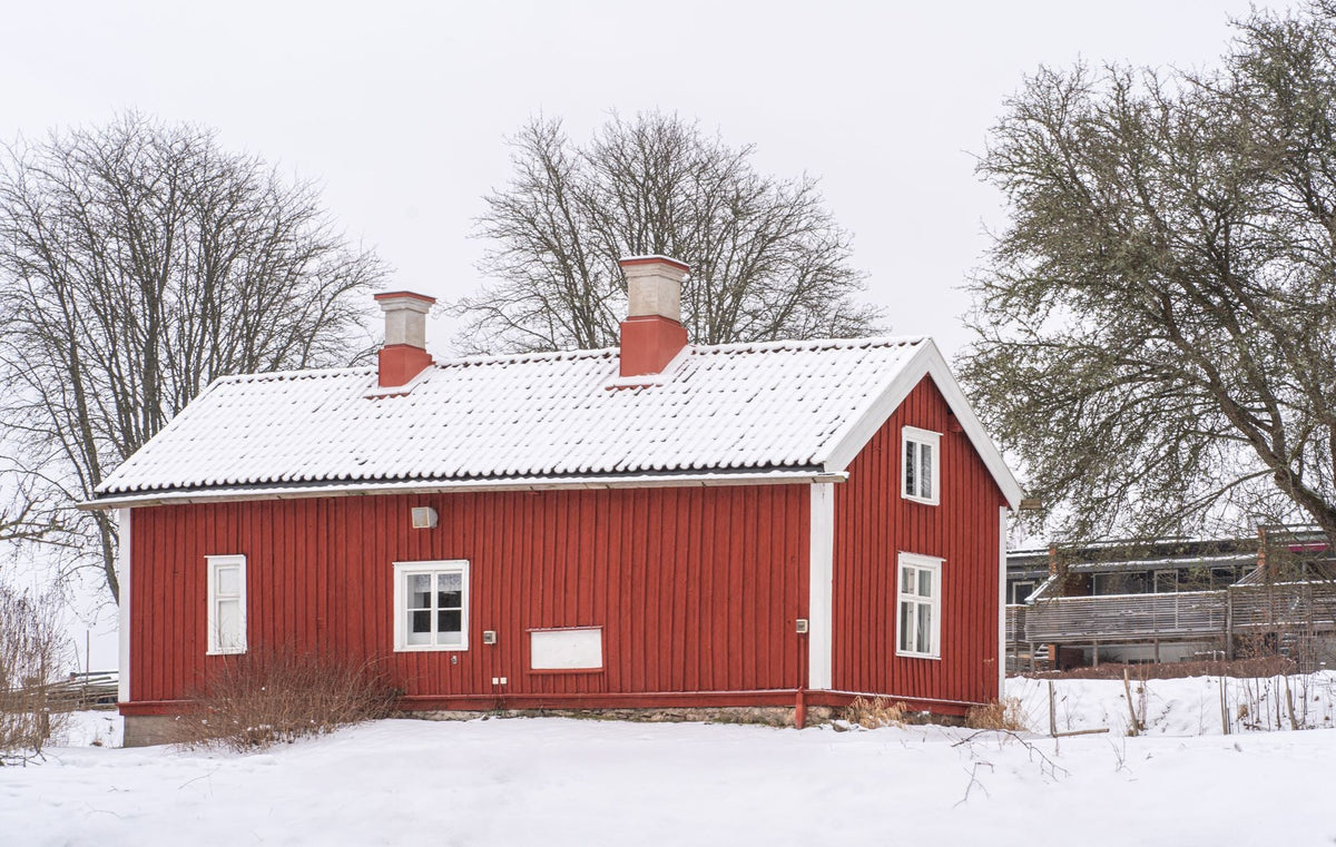Rött trähus med snötäckt tak på landsbygden under vintern